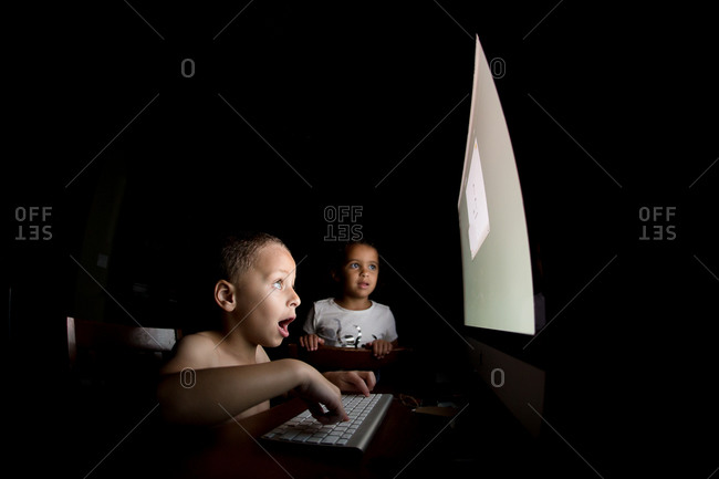 Young Girl Watches Boy Play On Computer In Dark Room Stock