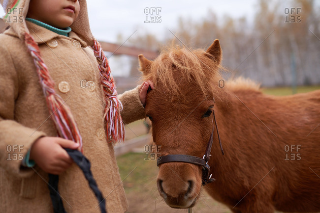 Girl in a winter overcoat standing next to a pony