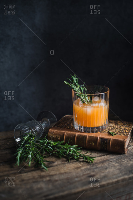 Orange cocktail garnished with rosemary sprig sitting on an old book