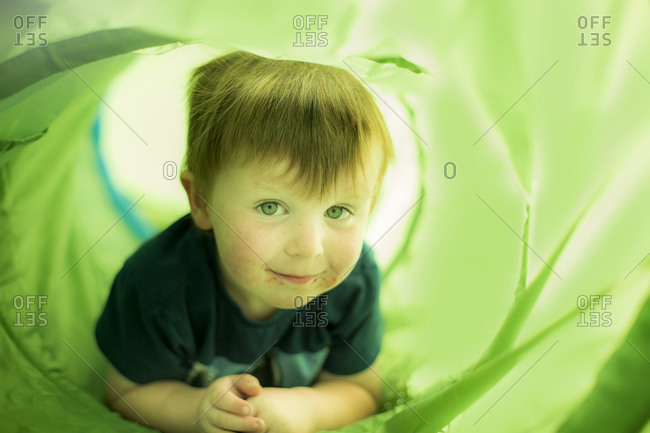 Smiling young boy crawling through green tunnel
