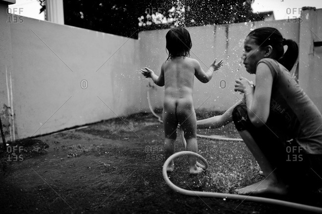 Woman spraying little boy with hose