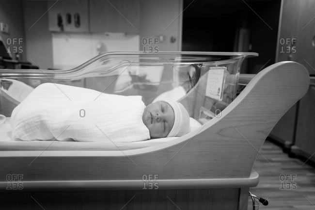 Newborn baby sleeping in hospital crib in black and white