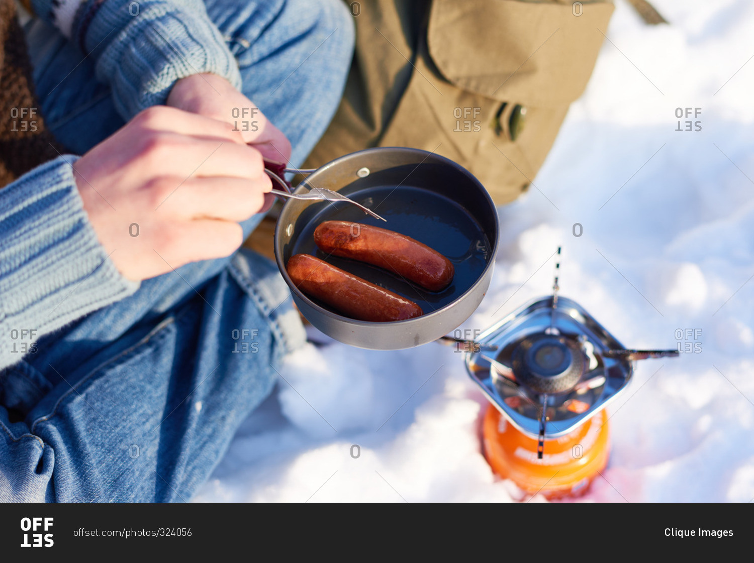 Man cooking sausages over a campstove in the snow