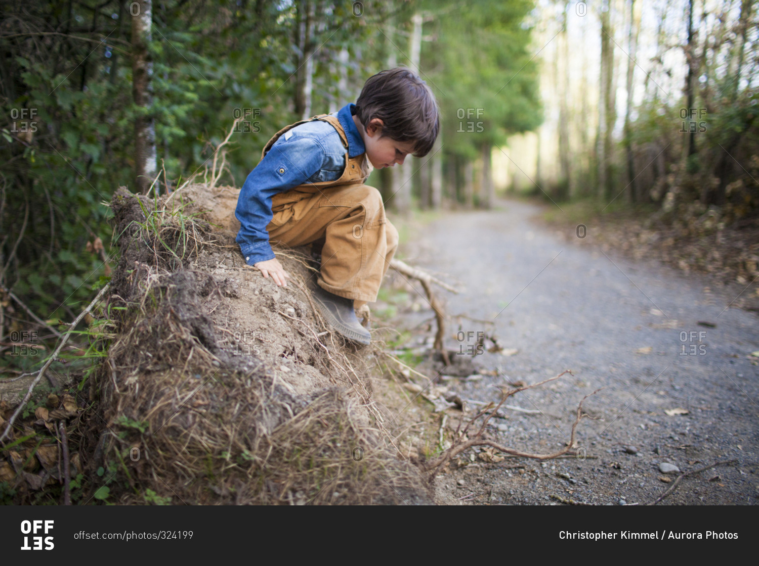 A young boy carefully plans to jump off a pile of dirt while playing outside