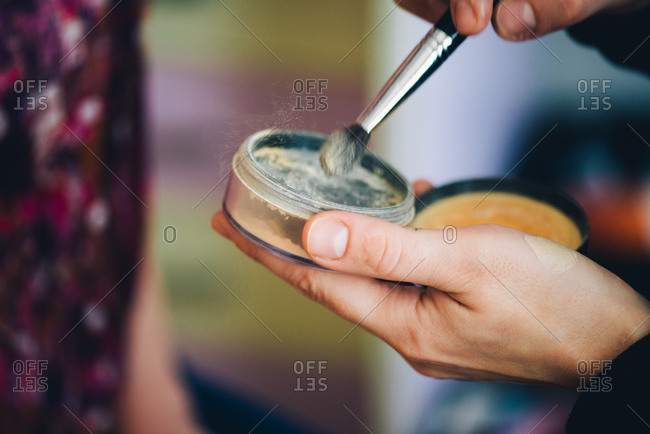 Person dipping makeup brush into powder makeup