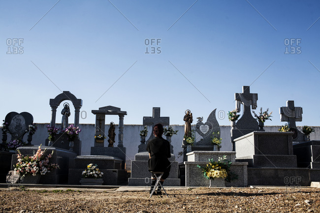 Woman sitting on a chair in a cemetery paying respect to the dead