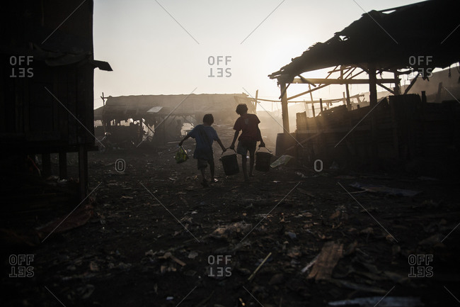 Two children carrying buckets through a slum in the Philippines