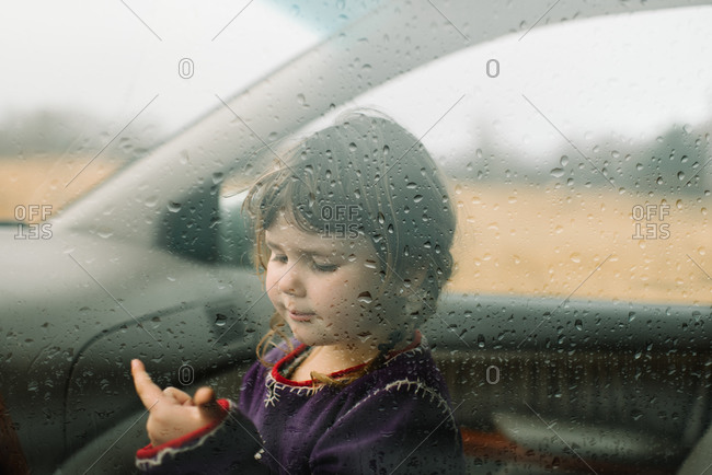 Young girl looking at moisture droplets on vehicle window