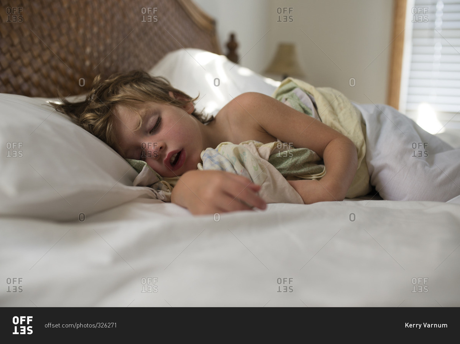 Little boy sleeping in bed with his armed wrapped around a blanket