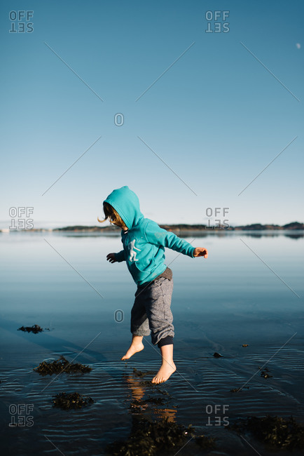 Kid in sweatshirt jumping over lake