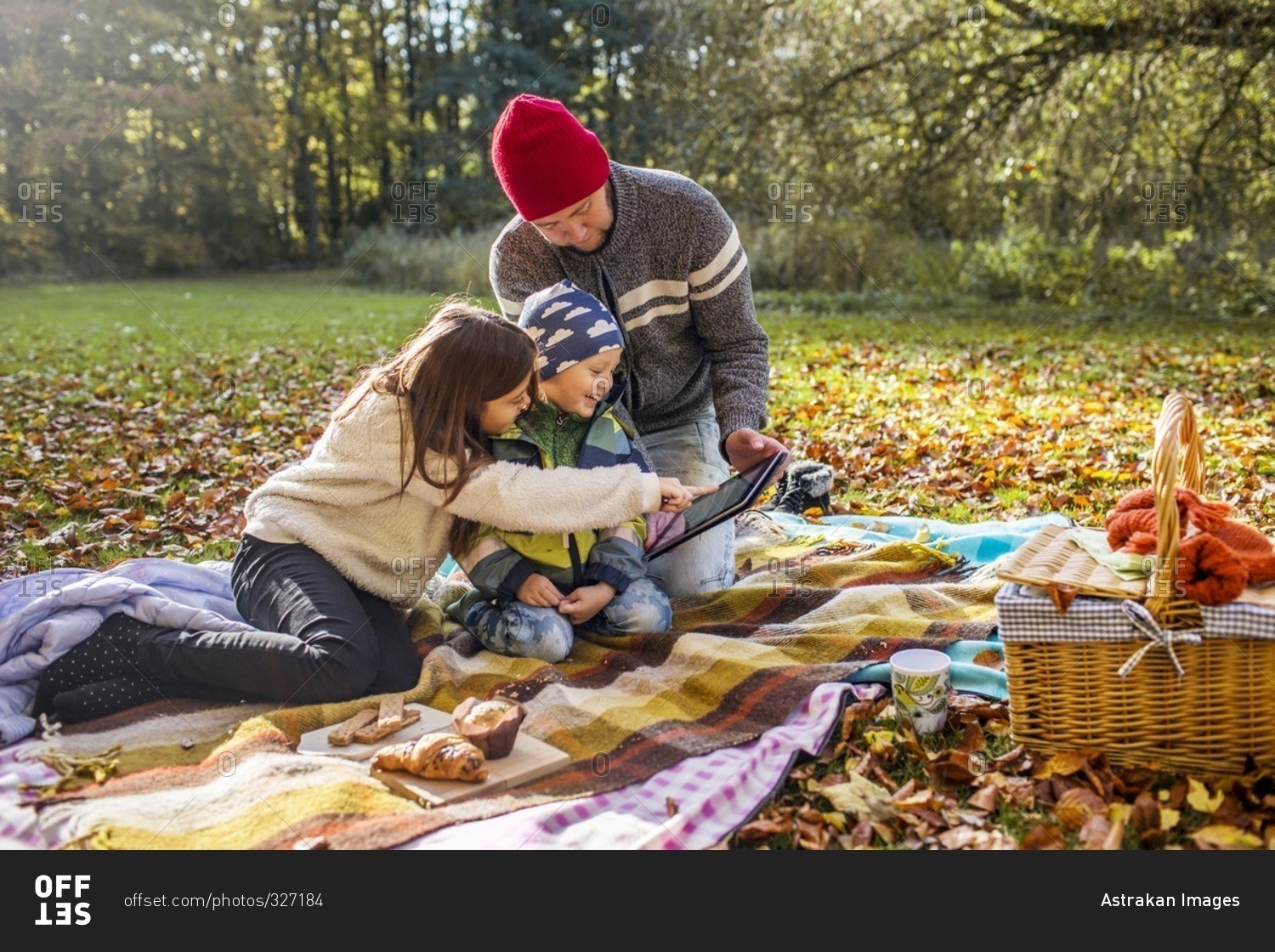 Father showing children tablet computer at autumn picnic