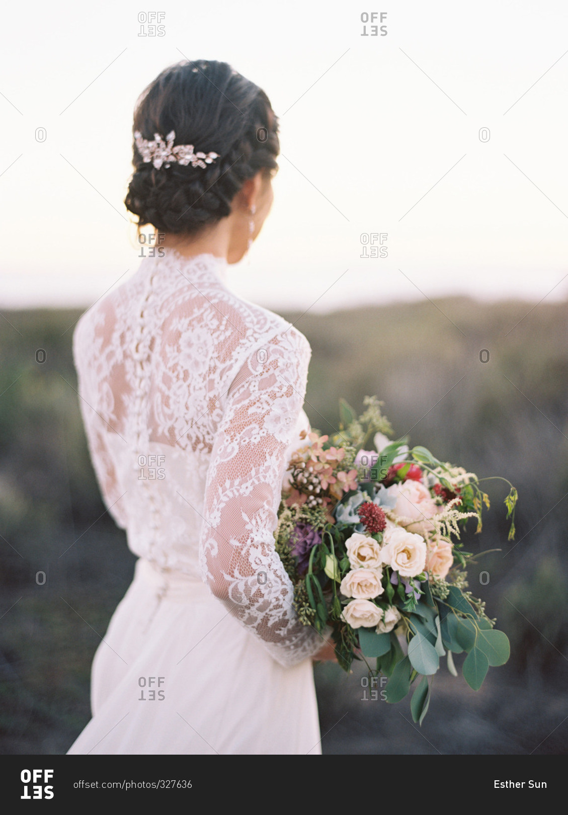 Bride holding bouquet, standing and looking out over the ocean