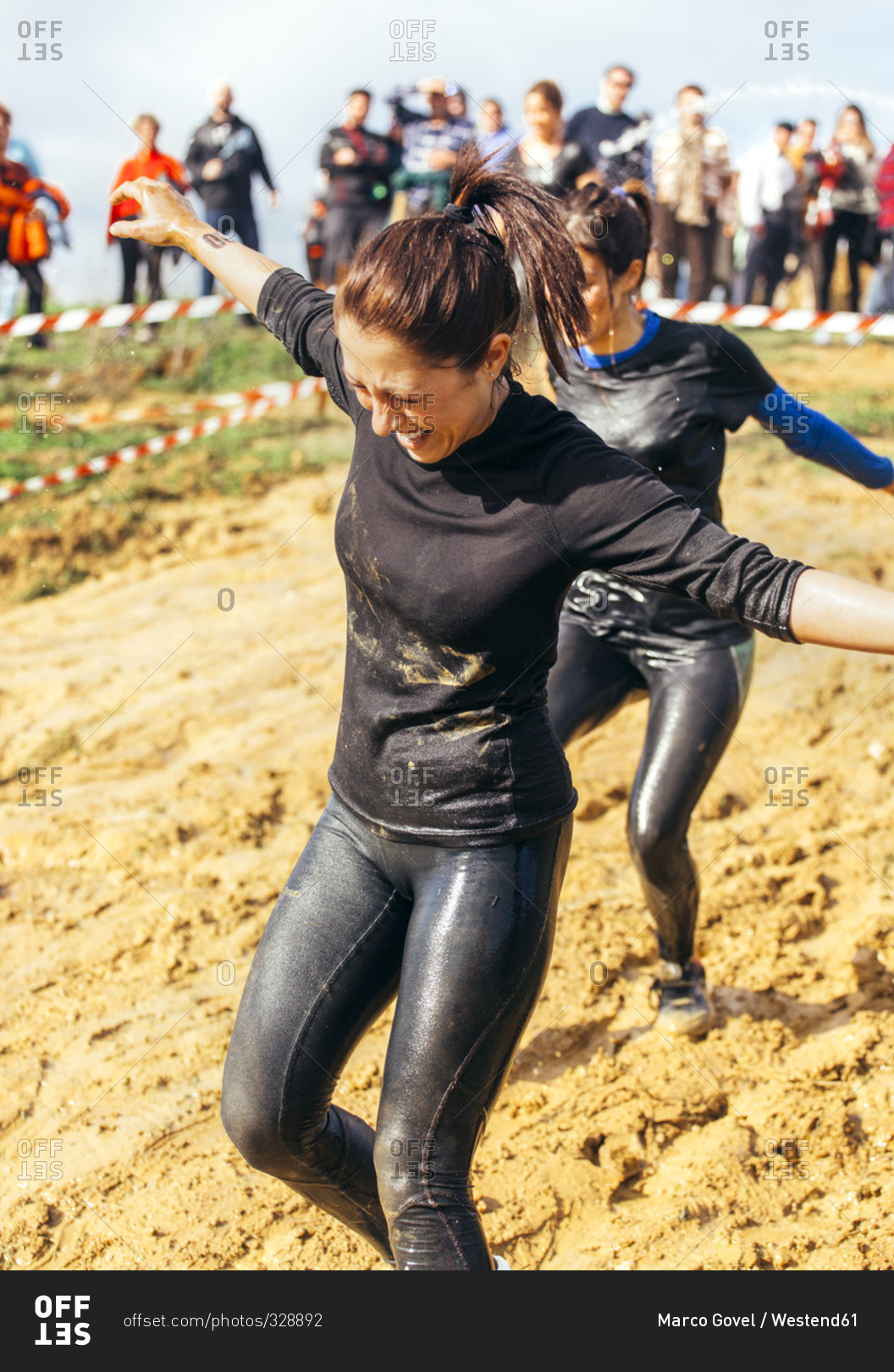 Two woman running through mud in an extreme obstacle race