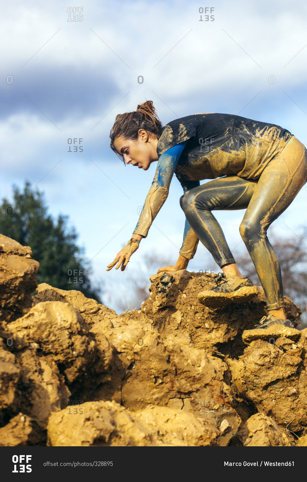 Woman in extreme obstacle race climbing down muddy rocks
