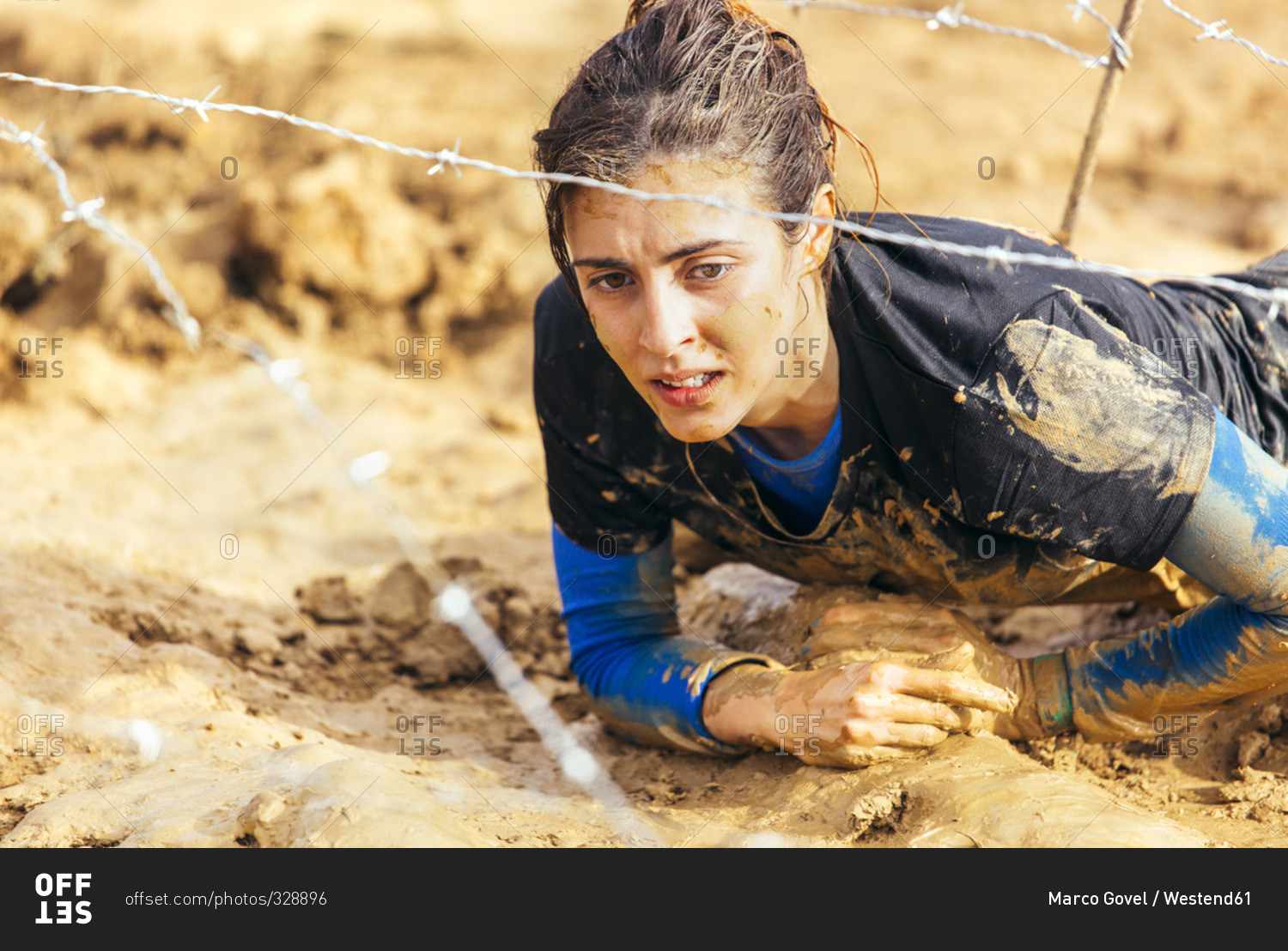 Woman in extreme obstacle race crawling under barbed wire