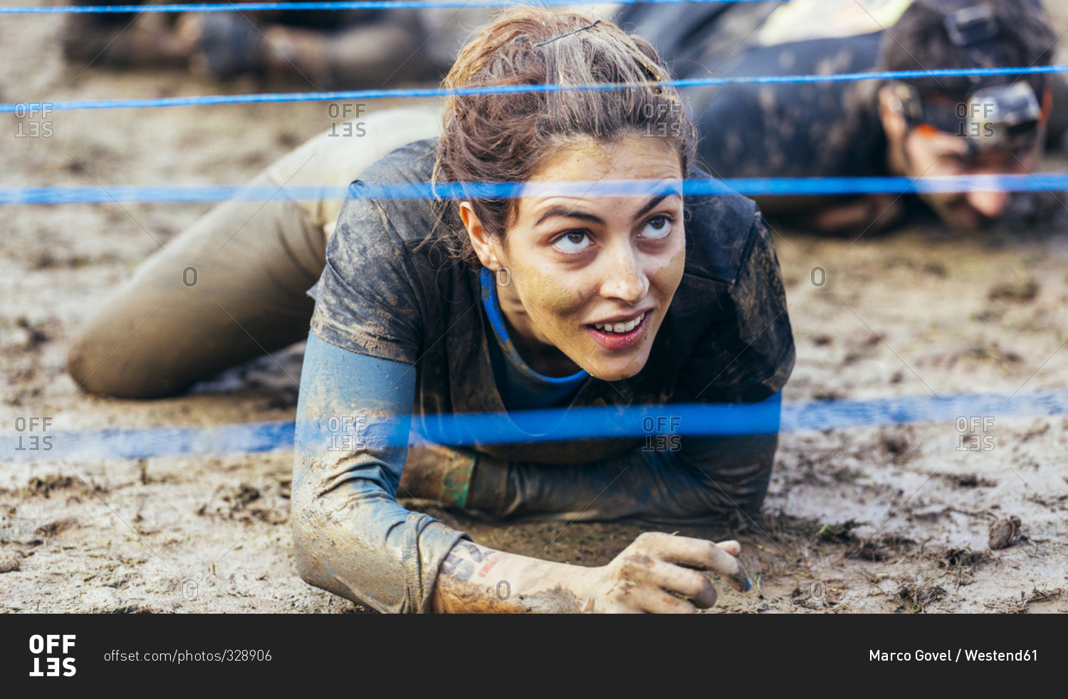 Woman in extreme obstacle race crawling under electric wire