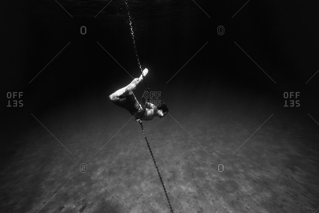 Young man underwater holding onto the anchor chain of a boat