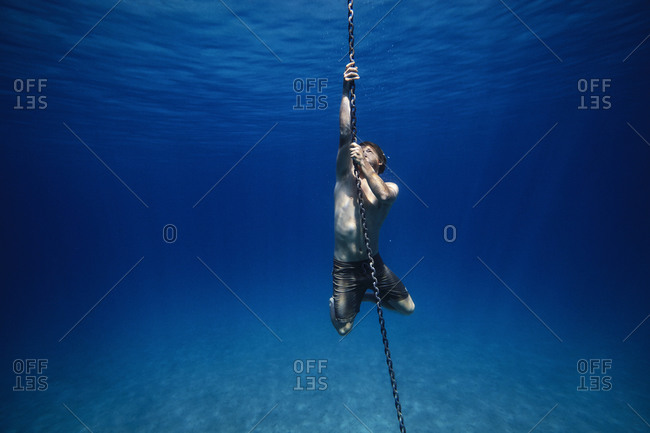 Young man holding onto an anchor chain underwater