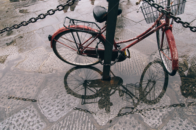 Bicycle locked to a post on a wet sidewalk