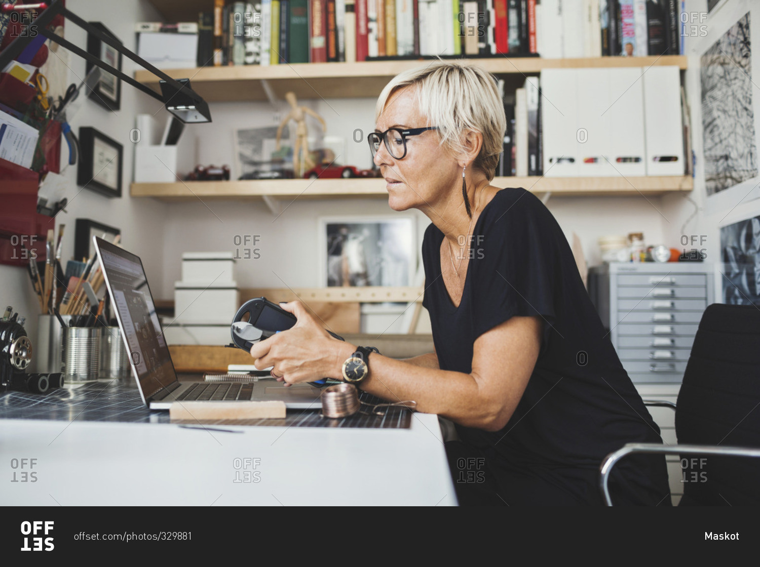 Female industrial designer using laptop while holding product at home office
