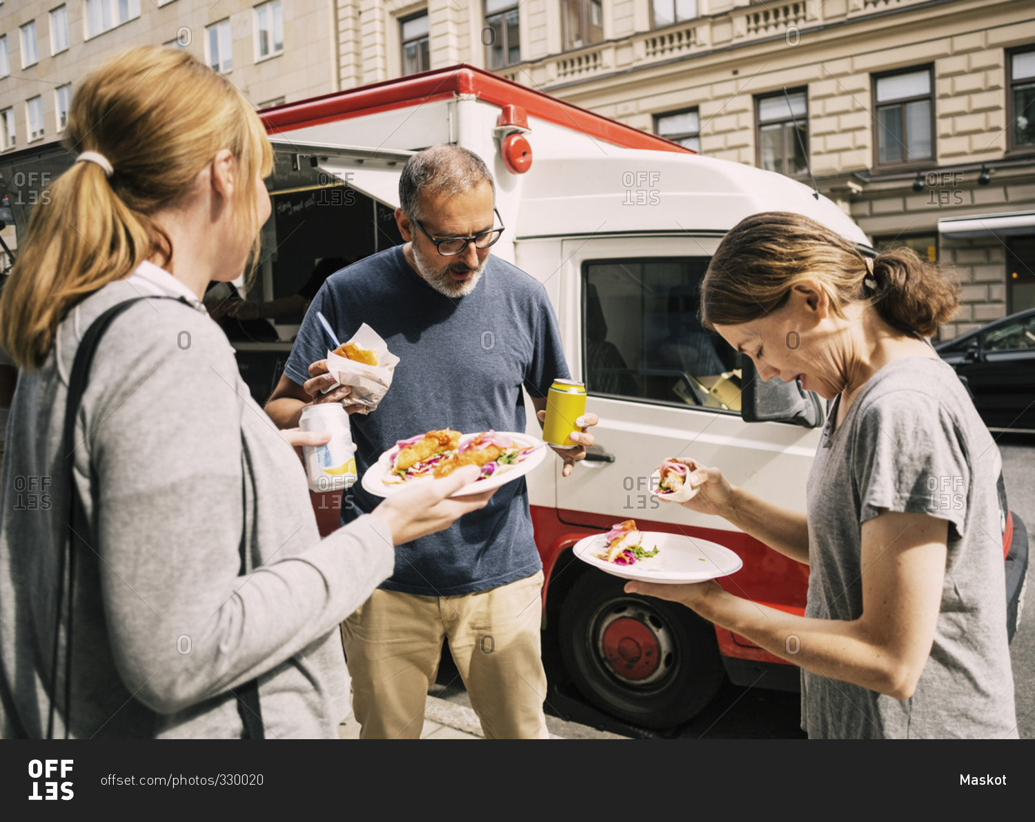 People eating food while standing by truck at city street