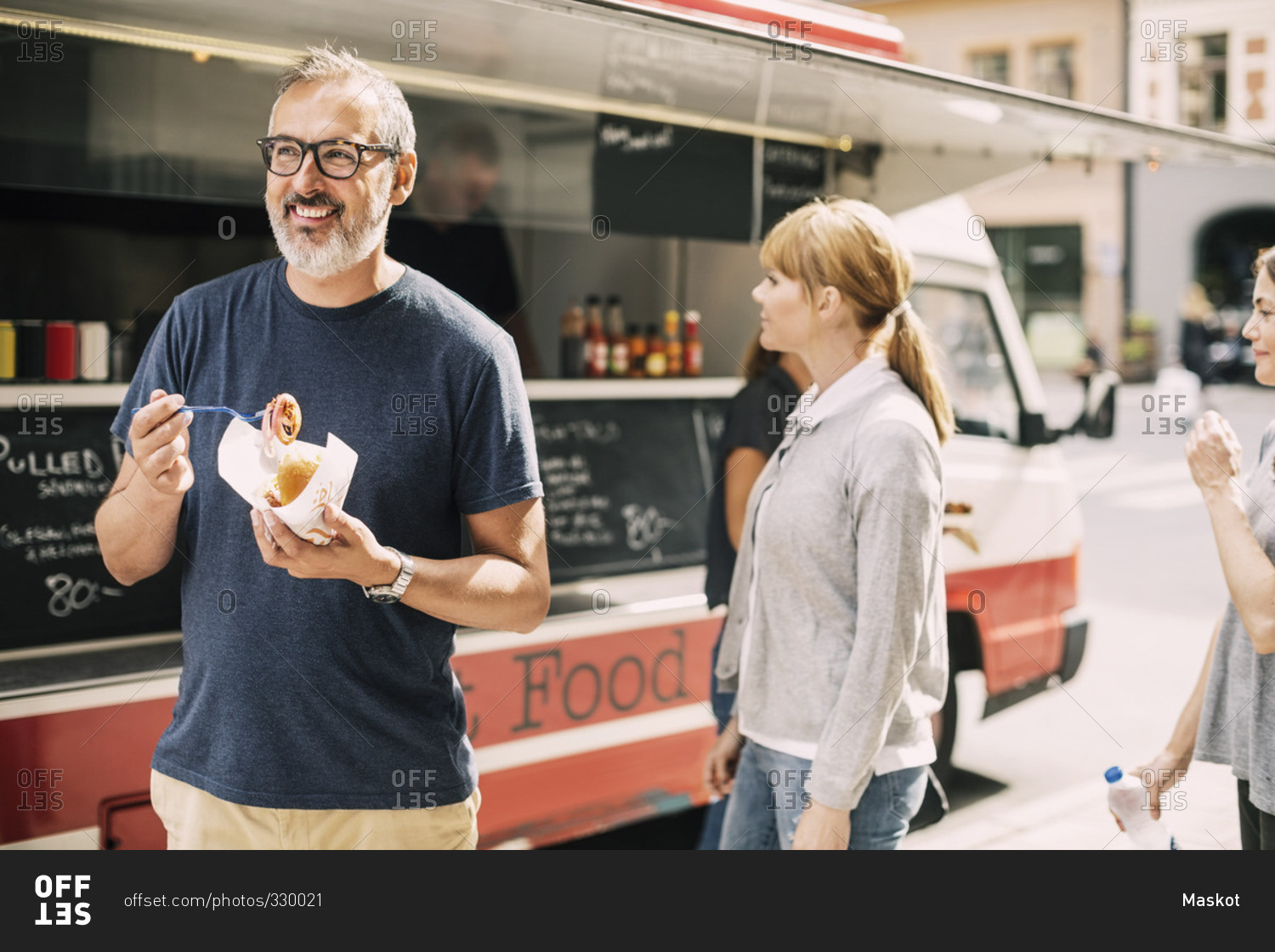 Mature man eating food while standing against truck at street
