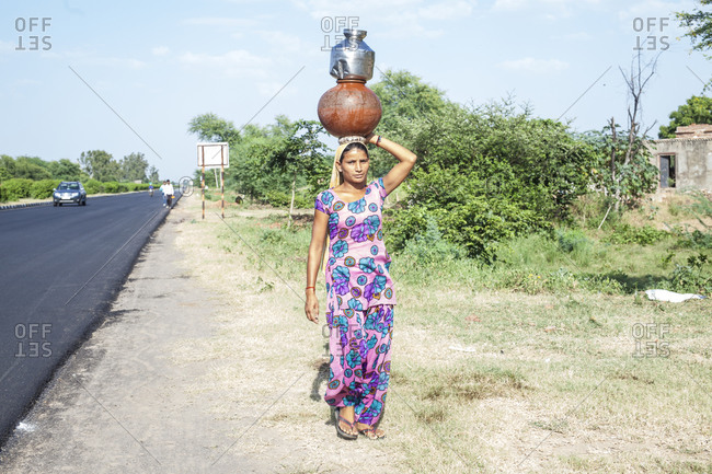 Agra, India - September 10, 2015: Woman walking along the roadside carrying water pots in Agra, India