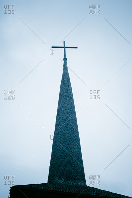 Wooden cross stands tall atop a pointed steeple of an old wooden church of St. John the Baptist, Brasov, Romania