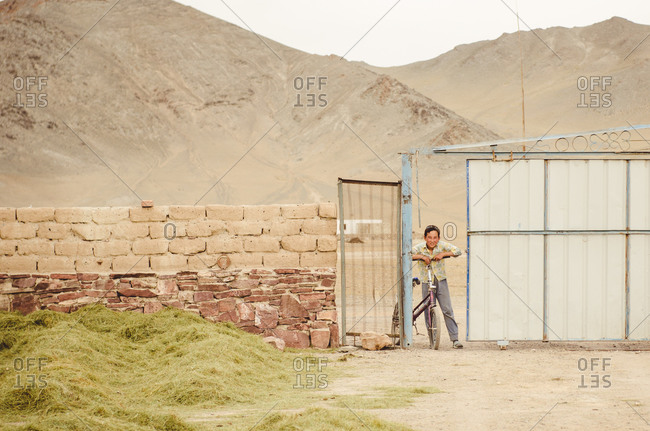 Mongolia - August 17, 2014: Smiling boy with bicycle at gate in Mongolia