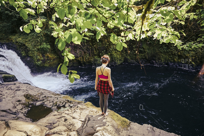 Woman standing on a rocky outcropping overlooking Punchbowl Falls in Oregon