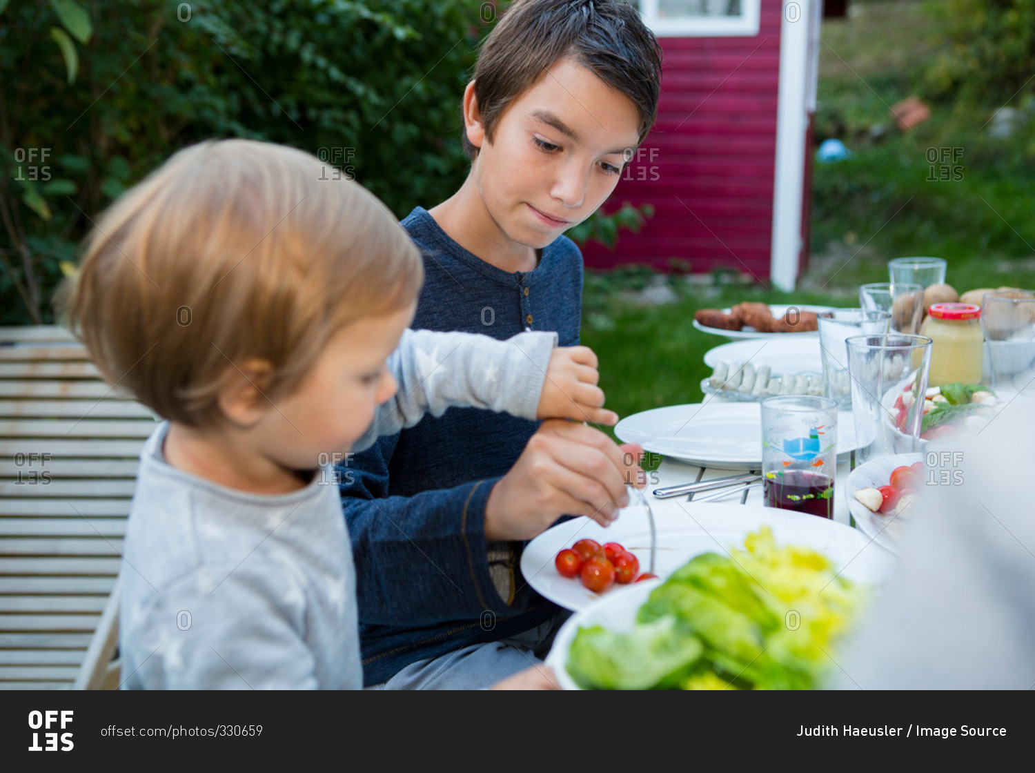 Teenage boy helping female toddler eat food at garden barbecue