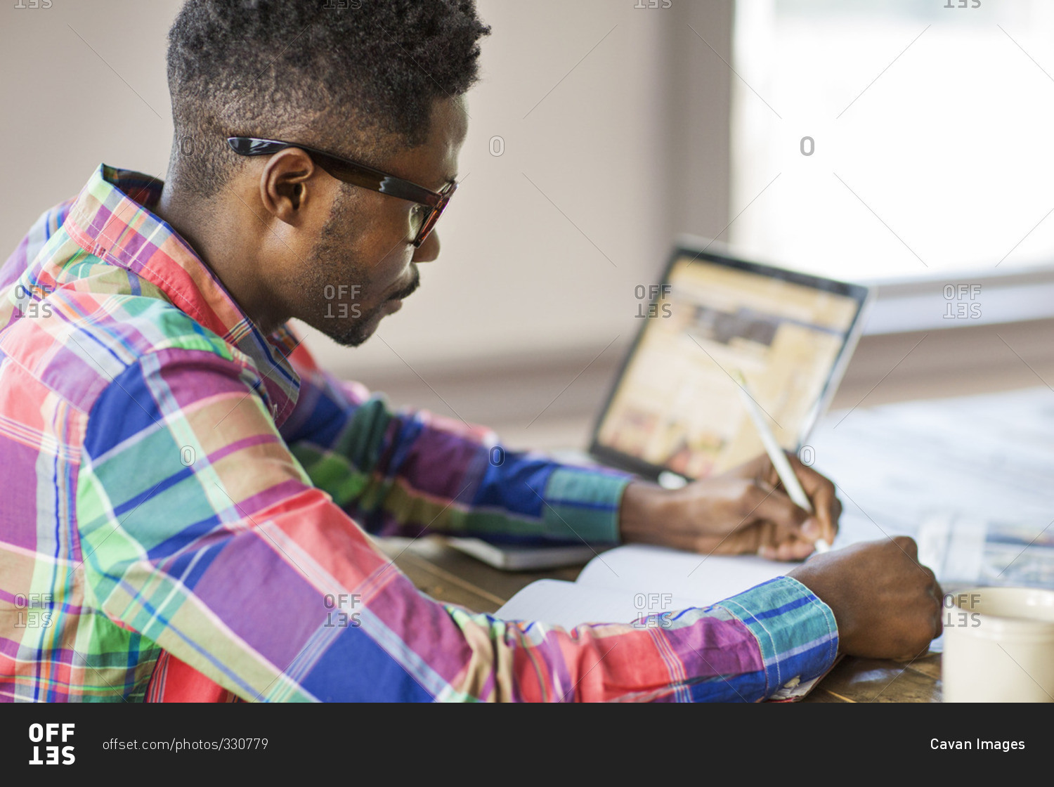 Man using a laptop and writing in a notebook