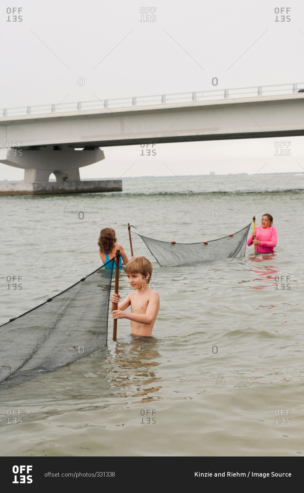 Children in ocean holding fishing nets and Sanibel causeway bridge