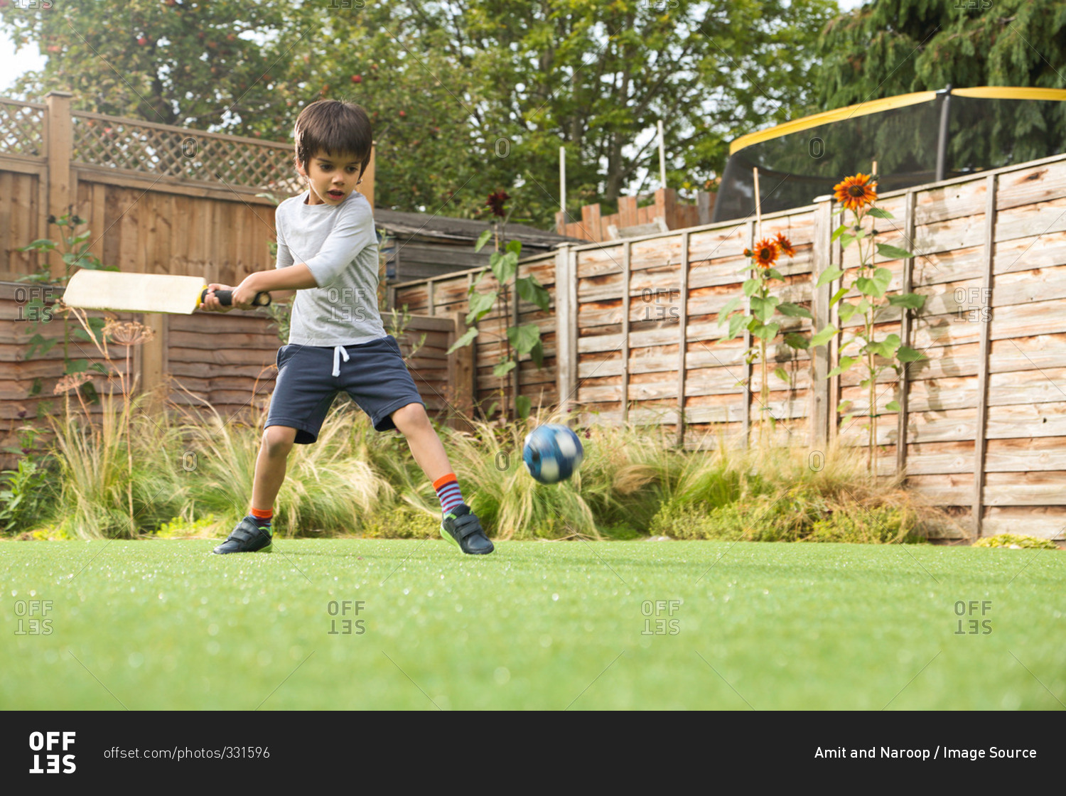 Boy playing cricket in garden with ball in mid air