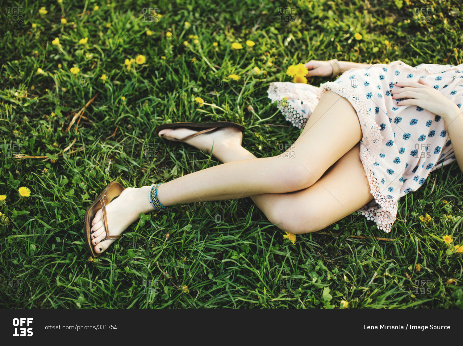 Waist down high angle view of young woman lying on grass wearing dress, flip  flops and ankle bracelet stock photo - OFFSET