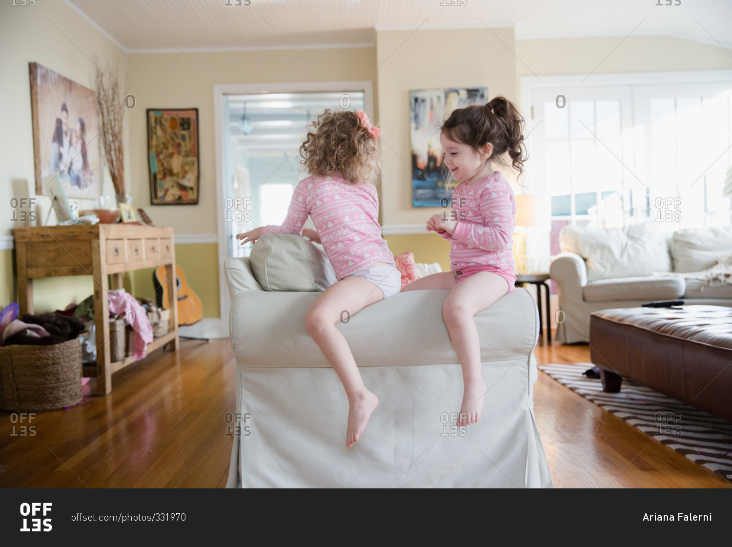 Two little girls in sitting on the arm of a sofa stock photo OFFSET