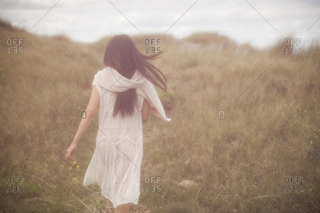 Woman in a sheer dress walking through tall grass towards the sea