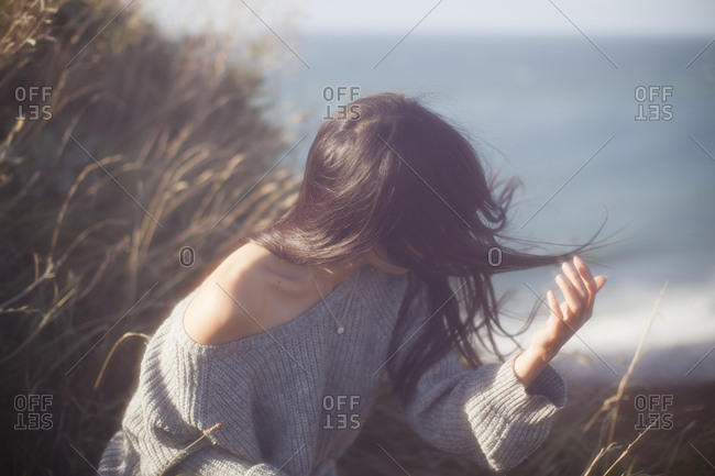 Woman sitting on a grassy, windswept dune near the sea