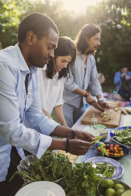 Multi-ethnic friends preparing food together at table in yard during summer party
