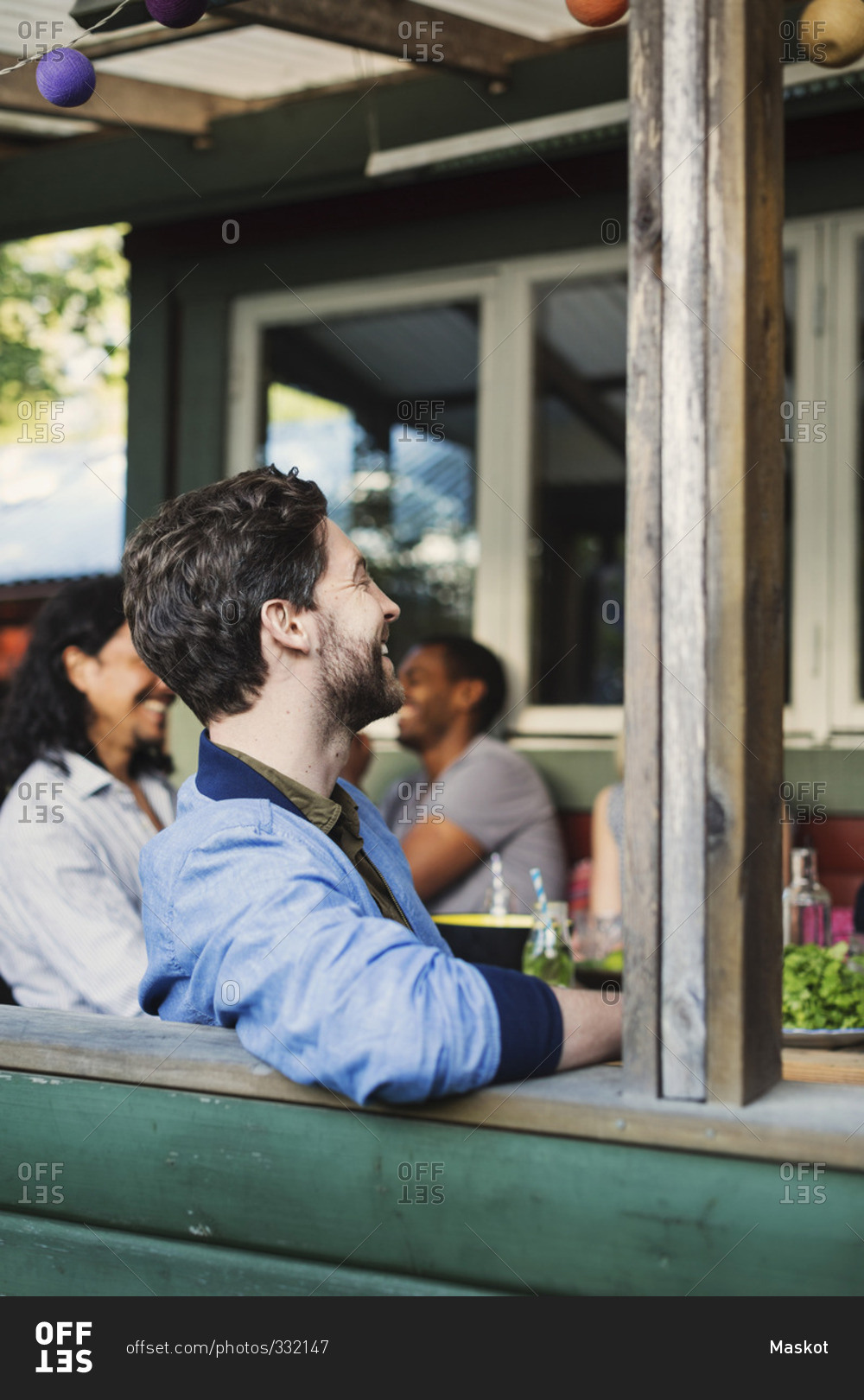 Side view of happy man sitting at porch while enjoying summer party with friends