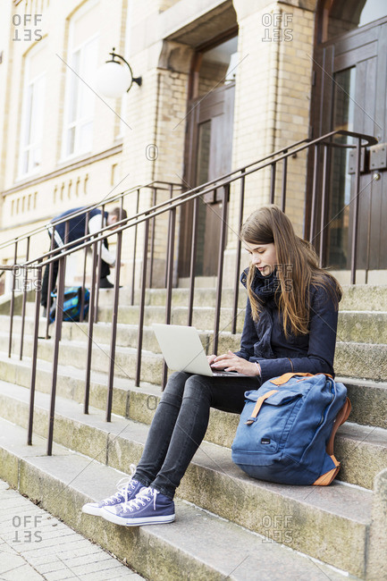 Young woman using laptop on steps of high school
