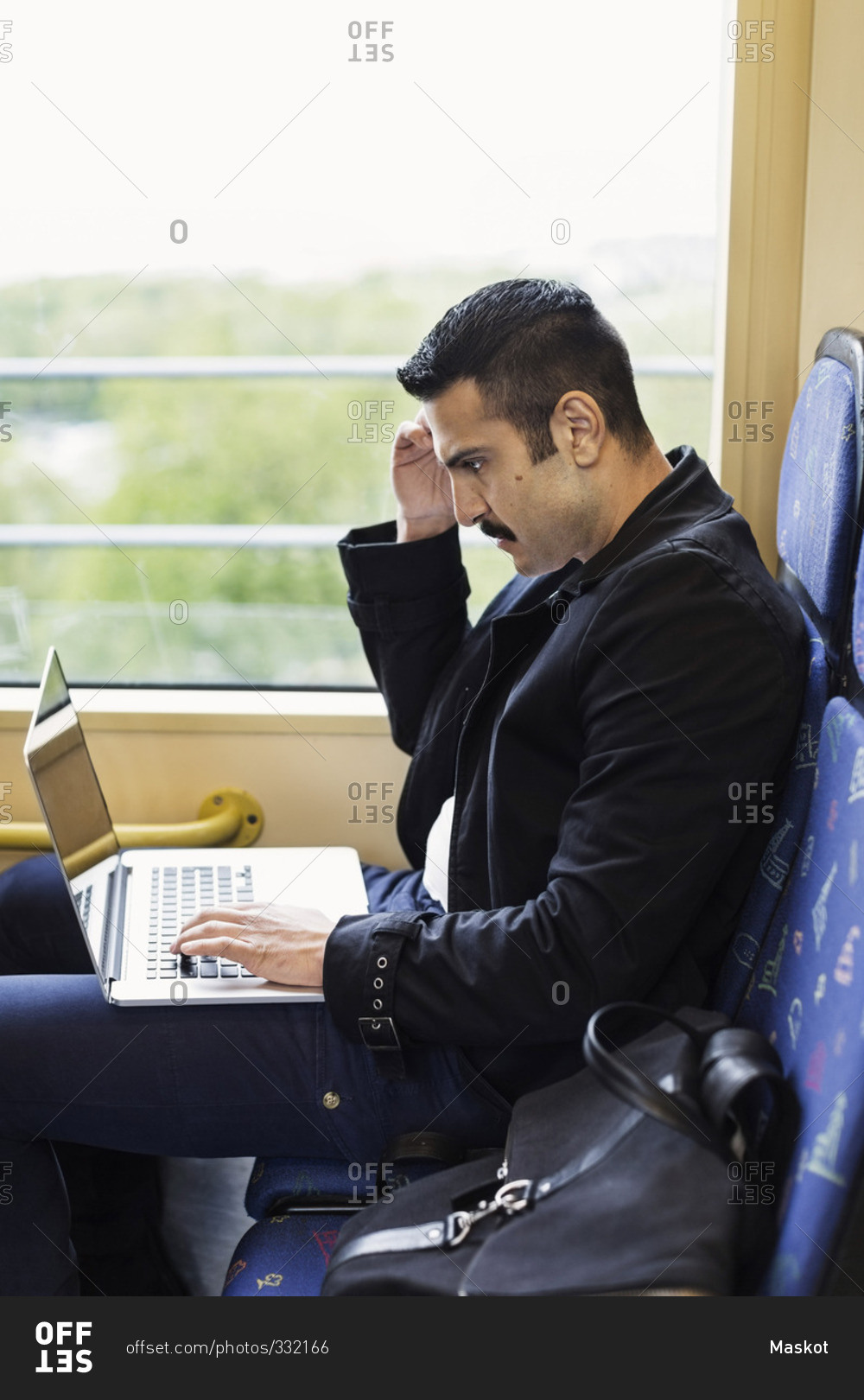 Side view of young man using laptop in tram