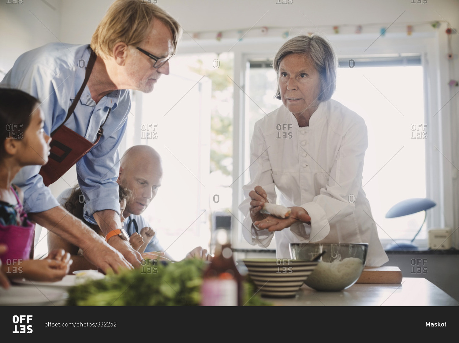 Senior woman teaching family to make Asian food in kitchen