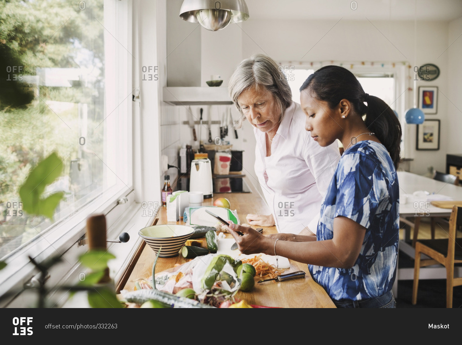 Senior woman using digital tablet with daughter-in-law while cooking food in kitchen
