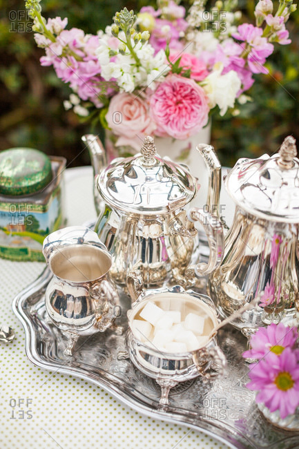 Silver tea service with pink flowers on table in garden