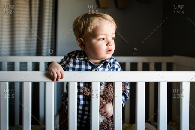 Portrait of a toddler boy standing with stuffed animal in crib