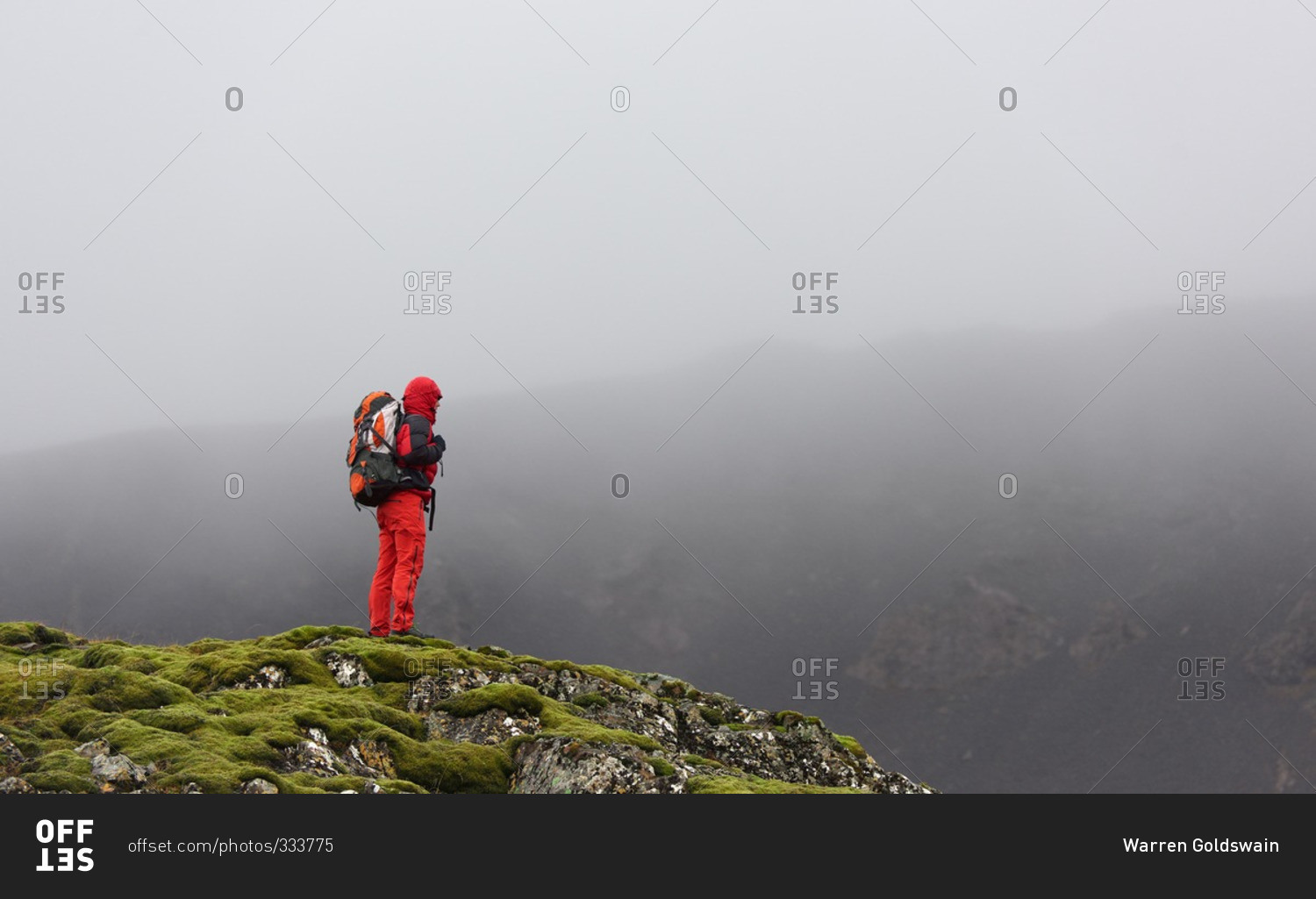 Hiker looking out into a valley on a mossy plateau with dark grey misty clouds in the background