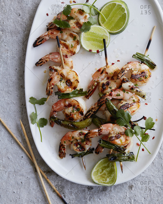 Shrimp skewers on a plate garnished with lime, cilantro and jalapeno