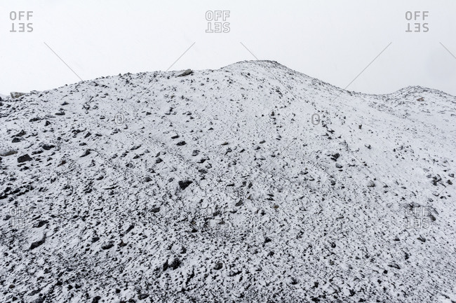A barren volcanic slope covered in snow during a storm