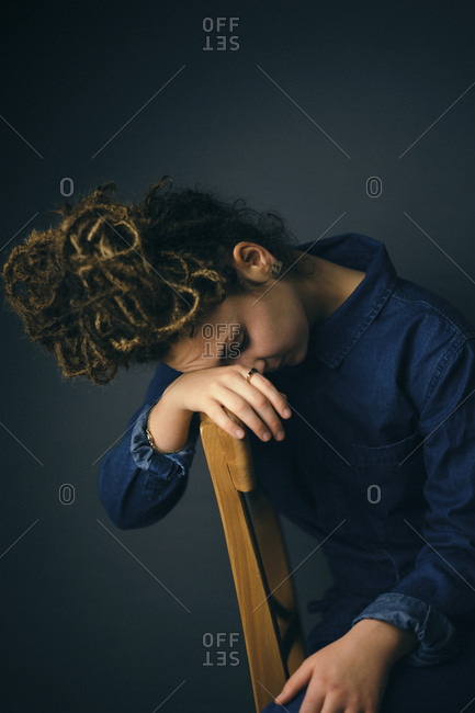 Woman sitting on a wood chair with her face buried in her hand